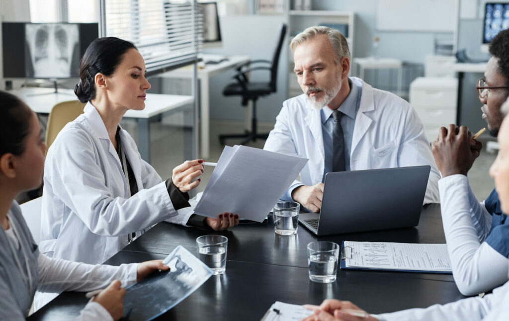 Young female clinician showing medical documents to experienced male doctor.