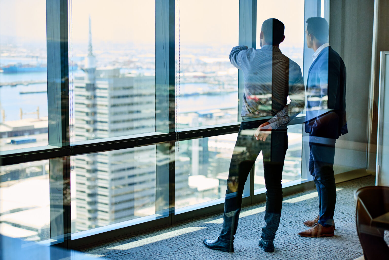 Two businessmen deep in discussion standing in front of windows in highrise building.