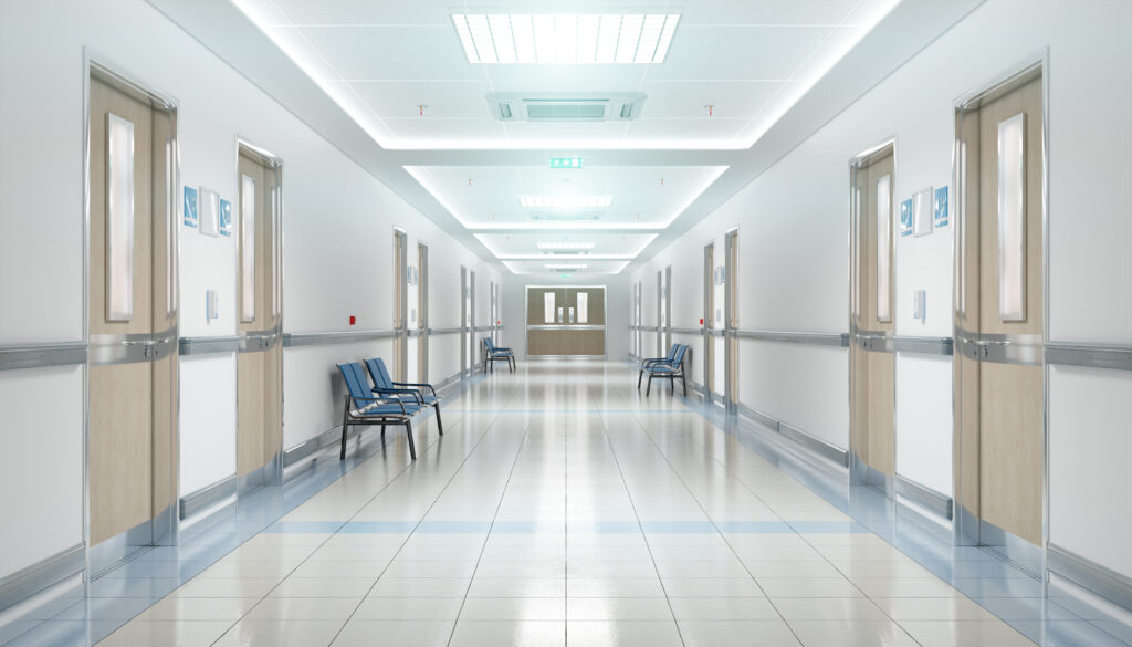 Long hospital bright corridor with rooms and blue seats.